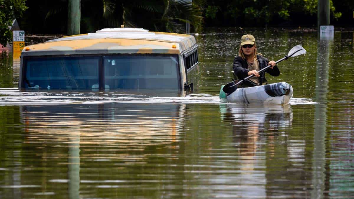 A man paddles his kayak alongside a submerged bus on a flooded street